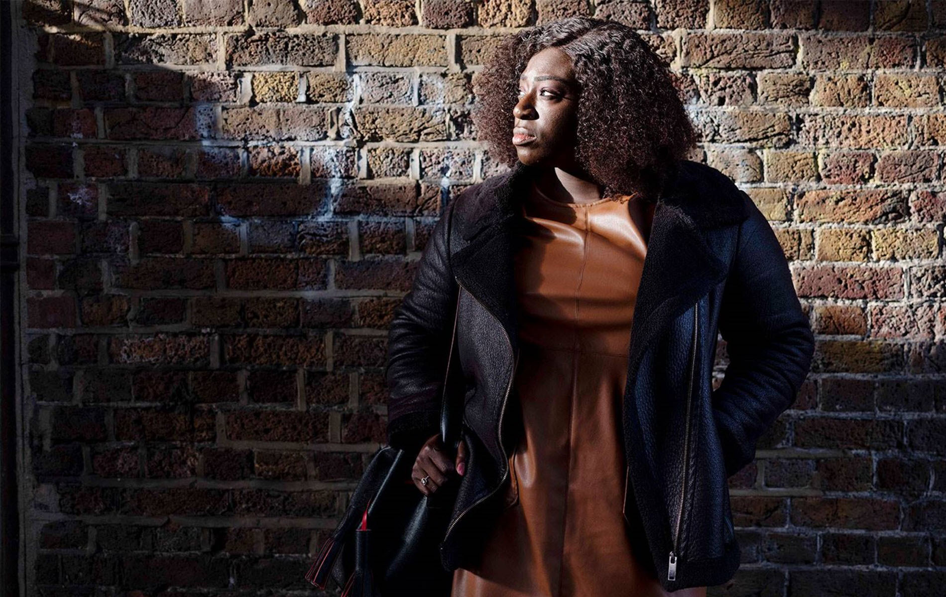 Photo of woman standing in front of a brick wall with the sun shining on her face